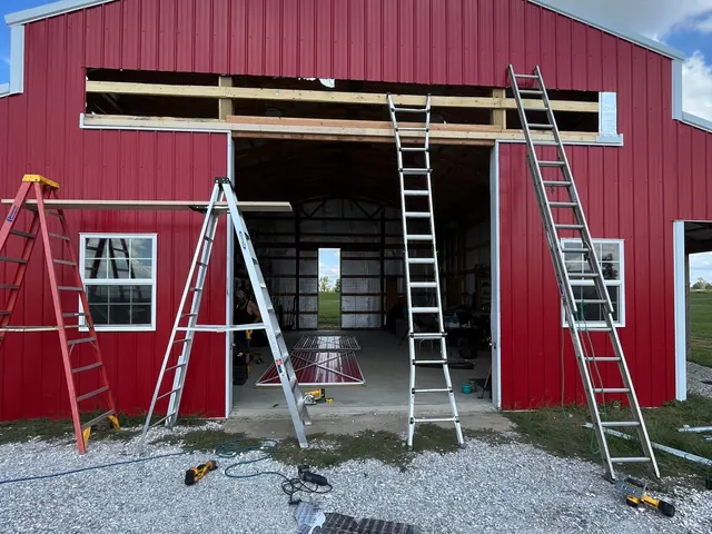 Red metal barn with ladders up for a door repair